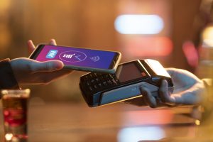 A person using their phone to make a contactless payment by tapping it on a digital payment terminal, highlighting the convenience of digital cards for fast transactions.