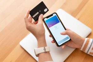 Close-up of a person holding a black credit card and a smartphone with a digital wallet app open, illustrating the digitalization on the US credit card system and the growing use of mobile payments with credit cards rewards.