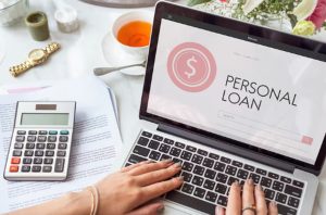 A person using a laptop displaying a personal loan application page, with documents and a calculator nearby, representing the process of applying for personal microloans online.