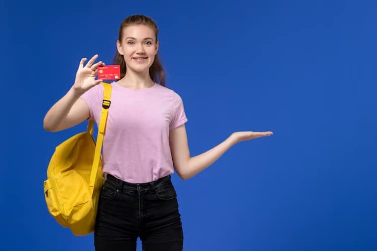 Smiling young woman with a backpack holding a red card and gesturing with her hand, representing the accessibility and appeal of student credit cards for managing personal expenses.