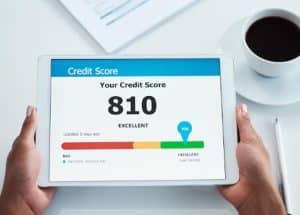 A person holding a tablet displaying a credit score of 810 marked as excellent, with a colorful credit range bar and a cup of coffee nearby on the desk. The screen emphasizes the importance of maintaining a high credit score for financial health.