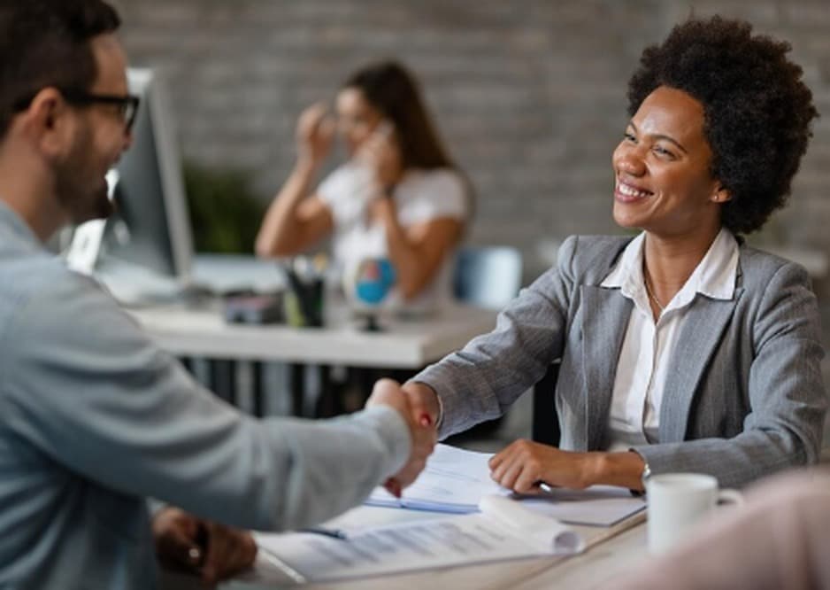 A smiling businesswoman shaking hands with a client in a professional office setting, with documents on the desk indicating a successful agreement or financial consultation related to lines of credit.
