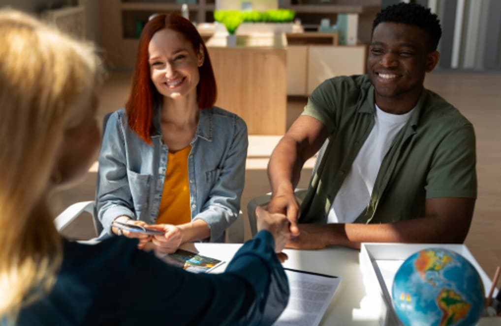 A smiling couple meeting with a financial advisor, shaking hands across a desk, representing trust and personalised services offered by community banks.