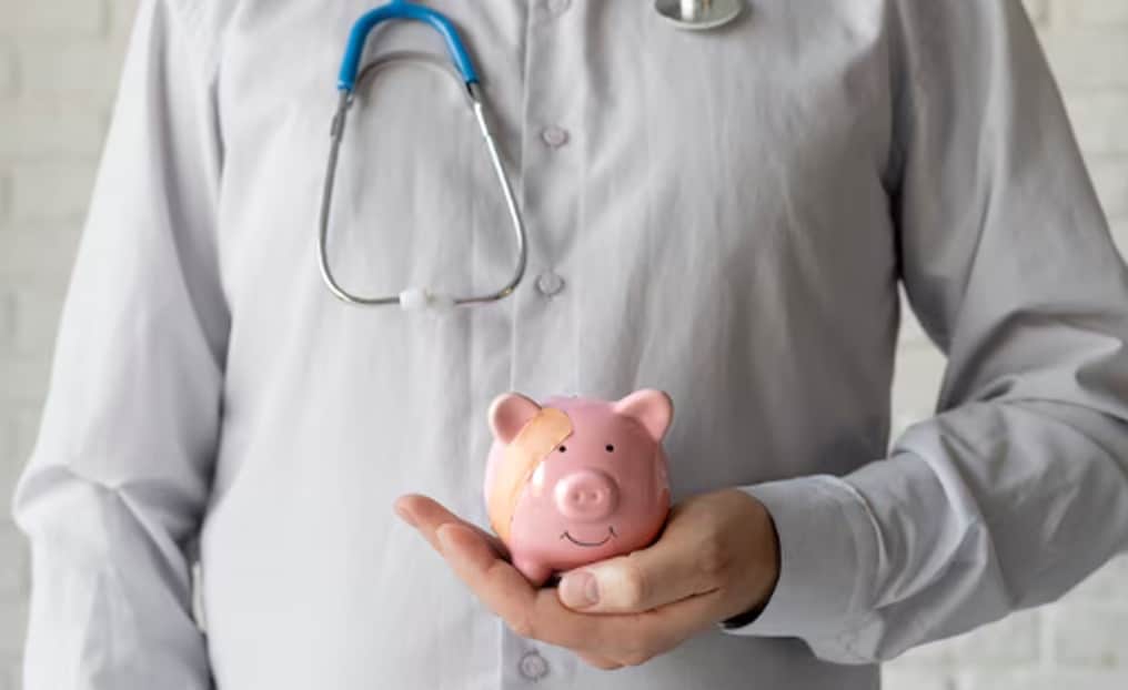A doctor holding a pink piggy bank with a plaster on it, symbolising financial support and the role of personal loans for medical emergencies.