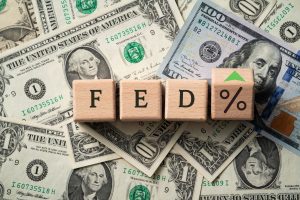 Wooden blocks spelling “FED” with a percentage symbol on dollar bills, representing the impact of changing Fed rates on the US economy and personal loans.